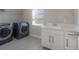 Well-lit laundry room equipped with modern appliances, custom cabinets, quartz countertops, and a stainless steel sink at 19554 Roseate Dr, Lutz, FL 33558