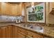 Close-up of a kitchen sink, granite countertops, and wooden cabinets with a bright window showing a large tree at 4926 Camellia S Way, St Petersburg, FL 33705