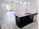 Kitchen island with granite countertop, sink, black cabinets, stainless steel dishwasher, and an adjacent living area with sliding doors at 5509 Cumberland Star Ct, Lutz, FL 33558