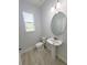 Clean and modern powder room with a pedestal sink, round mirror, and a window providing natural light at 5509 Cumberland Star Ct, Lutz, FL 33558