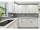 Kitchen with white cabinetry, gray countertop, herringbone backsplash and stainless steel sink at 1236 Abbey Crescent Ln, Clearwater, FL 33759