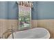 Standalone tub with fixtures, a window with blinds, and neutral colored tiles at 16420 Iola Woods Trl, Dade City, FL 33523