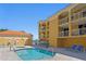 Brightly lit community pool with blue lounge chairs, a spa, and yellow buildings in the background at 5353 Gulf Blvd # B103, St Pete Beach, FL 33706