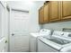 Well-lit laundry room featuring a white washer and dryer set, wood cabinets, and a door to the side yard at 8116 Sanguinelli Rd, Land O Lakes, FL 34637