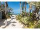 Sandy beach access path leading to the ocean with lush tropical landscaping and palm trees for shade at 122 10Th Ave, Indian Rocks Beach, FL 33785
