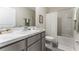 Bright bathroom boasts a white vanity, marble countertop, toilet and tiled shower with a glass door at 33105 Major Oak Dr, Wesley Chapel, FL 33545