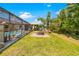 Well-manicured backyard featuring a fire pit, lush lawn, and a screened-in pool area at 18836 Green Park Rd, Hudson, FL 34667