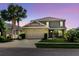 Charming two-story home featuring a well-manicured lawn, palm trees, and an attached two-car garage at dusk at 27094 Carolina Astor, Wesley Chapel, FL 33544
