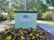Community entrance sign for 'The Woods', surrounded by colorful landscaping at 7039 Woodibis Dr, New Port Richey, FL 34654