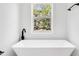 Bright bathroom features a white freestanding tub and a black faucet with a nature view from the window at 7113 S Kissimmee St, Tampa, FL 33616