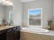 Elegant bathroom featuring a soaking tub, granite counters, dark cabinets, and a large window at 7927 Hampton Lake Dr, Tampa, FL 33647