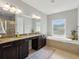 Luxurious bathroom with double sinks, a soaking tub, granite countertops, and dark wood cabinets at 7927 Hampton Lake Dr, Tampa, FL 33647
