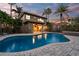 Twilight view of a backyard pool with blue water reflecting the house lights, surrounded by lush landscaping and a paved deck at 6315 Marbella Blvd, Apollo Beach, FL 33572