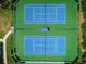 Aerial view shows dual tennis courts featuring blue playing surfaces surrounded by well-maintained green grounds at 2629 Timacqua Dr, Holiday, FL 34691