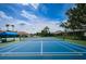 A blue tennis court features a shaded seating area and well maintained green surface within the residential community at 2629 Timacqua Dr, Holiday, FL 34691