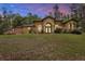 An elegant one-story home with beige stucco, an arched entryway, and mature landscaping on a sprawling lawn at 24498 Casey Rd, Brooksville, FL 34601