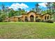 An elegant one-story home with beige stucco, an arched entryway, and mature landscaping on a sprawling lawn at 24498 Casey Rd, Brooksville, FL 34601