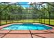 A bright blue swimming pool is surrounded by a brick patio inside a screened enclosure overlooking a grassy, wooded yard at 24498 Casey Rd, Brooksville, FL 34601