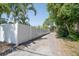 Long gravel driveway leading alongside a tall white fence with palm trees and lush foliage at 7301 2Nd S Ave, St Petersburg, FL 33707
