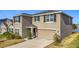 View of the two-story home with beige paint, black shutters, two-car garage, and landscaping at 7782 Sail Clover Ln, Zephyrhills, FL 33540