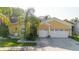 Exterior view of a yellow two-story home with a well-manicured lawn, landscaping, and a three-car garage at 11209 Pocket Brook Dr, Tampa, FL 33635