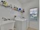 Laundry room with white washer, dryer, sink, shelving with detergents, and natural light from a window at 13421 Sydney Rd, Valrico, FL 33594
