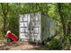 Practical storage container in the wooded backyard with a red hand truck, great for organization and accessibility at 9019 Stone Dr, Webster, FL 33597