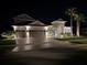 Exterior elevation of home at night featuring a three-car garage, manicured lawn, and palm trees at 32791 Natural Bridge Rd, Wesley Chapel, FL 33543