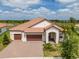Attractive single-story home showcasing a tile roof, a brick driveway, a three-car garage, and tropical landscaping at 5329 Windy Grove Dr, Wimauma, FL 33598
