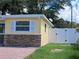 A yellow home with a brick facade with a white vinyl fence, and well-maintained green grass in the backyard at 844 67Th S St, South Pasadena, FL 33707