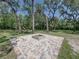 Brick patio with a brick fire pit in the center, surrounded by shade trees and green grass at 13004 Bell Creek Chase, Riverview, FL 33569