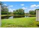 Backyard with grass lawn offering a peaceful waterfront view and blue skies dotted with clouds, framed by lush trees at 6831 Dartmouth Hill St, Riverview, FL 33578