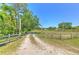 A long gravel drive leads through a rustic gate and wooden fence towards the beautiful acreage at 7509 Hackamore Rd, Zephyrhills, FL 33541