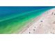 Breathtaking aerial view of a sandy beach meeting the clear blue ocean, dotted with beach umbrellas and people at 19925 Gulf Blvd # 503, Indian Shores, FL 33785