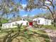 Beautiful single-story home with a striking red door and manicured front lawn, surrounded by mature trees at 2947 Cedar Trce, Tarpon Springs, FL 34688