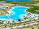 An aerial view of a neighborhood lagoon with swimming areas, waterslides, beaches, and lounge areas under palm trees at 7486 Tuscan Bay Cir, Wesley Chapel, FL 33545