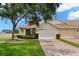 Charming single-story home with well-manicured lawn, mature tree, and brick driveway leading to a two-car garage at 2309 New Orchard Ct, Sun City Center, FL 33573
