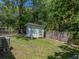 Fenced backyard featuring a small storage shed, green grass, and lush green trees at 131 Oak Park Ave, Brooksville, FL 34601