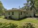 Back exterior of a green house featuring lush green grass, an AC unit, and a back porch at 131 Oak Park Ave, Brooksville, FL 34601