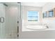 All-white bathroom featuring a glass shower and soaking tub with a window at 14623 Horse Trot Rd, Lithia, FL 33547