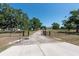 View of the home entrance featuring a driveway gate, mature trees, green grass and blue skies at 4416 Tevalo Dr, Valrico, FL 33596