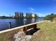 Tranquil waterfront view of condos with a bench, lush greenery, and clear blue skies at 600 Gardens Edge Dr # 614, Venice, FL 34285