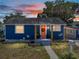 Charming blue single-story home with a welcoming coral-colored front door and sunset sky at 10562 Lake Dr, Seminole, FL 33772