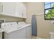 Bright laundry area with white washer, dryer, cabinets, and view from the black-framed window at 1341 Marinella Dr, Palm Harbor, FL 34683