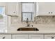 Close-up of a kitchen sink with a stainless steel faucet, white cabinets, and stone tile backsplash at 232 Hunter Ct, Palm Harbor, FL 34684