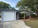 Single story home featuring an attached garage, red door, tropical landscaping and mature trees at 1542 Sherwood St, Clearwater, FL 33755