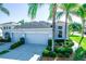 Light blue home featuring a three-car garage, well-manicured bushes, and elegant palm tree landscaping at 1257 Lyndhurst Greens Dr, Sun City Center, FL 33573