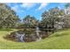 Scenic view of the community pond featuring a central fountain and surrounded by mature trees and grassy banks at 2650 Countryside Blvd # A104, Clearwater, FL 33761