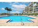 Community outdoor pool with clear water, condo building, palm trees, lounge chairs, and beautiful blue sky view at 7872 Sailboat Key S Blvd # 306, South Pasadena, FL 33707