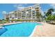 Community outdoor pool with view of a large condo building with many balconies, palm trees, and blue sky view at 7872 Sailboat Key S Blvd # 306, South Pasadena, FL 33707